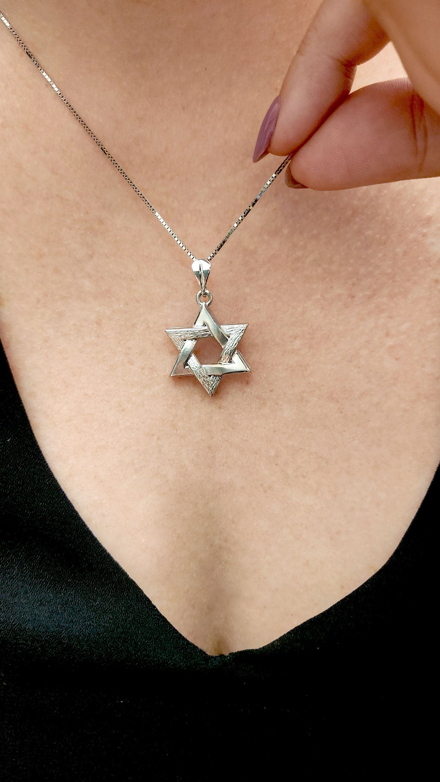 a woman is holding a star of david necklace